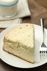 Piece of delicious sponge cake and fork on wooden table, closeup
