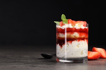 Tasty trifle dessert. Strawberries, sponge cake and whipped cream in glass on grey table, space for text
