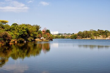 A photo of a still lake surrounded by green park landscape   and the bustling city skyline in the background, taken during the golden hour.