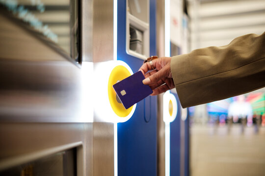 Female hand holding a card on a contactless reader machine in train station.