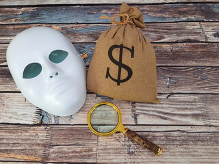 Bag of money, magnifying glass and mask on an old wooden table.
