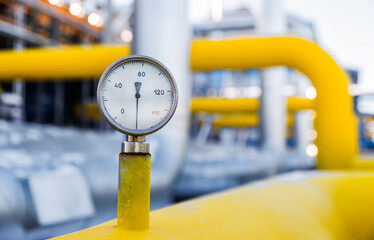 A pressure gauge prominently displays measurements on a yellow pipe in a bustling gas processing...
