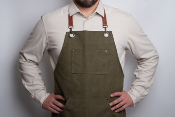 A man in a kitchen apron. Chef work in the cuisine. Cook in uniform, protection apparel. Job in food service. Professional culinary. Green fabric apron, casual stylish clothing. Handsome baker posing