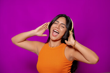 Energetic woman singing along to music with yellow headphones, eyes closed and smiling brightly, enjoying the moment against a purple background. 