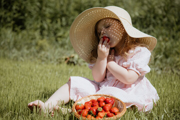 The Joyful Little Girl in a Straw Hat Enjoying Fresh Strawberries in a Sunlit Summer Meadow