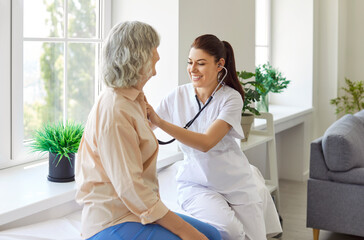 Young woman nurse or doctor stethoscope examining old senior patient, GP checking heartbeat at...