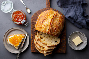 Sourdough bread on wooden cutting board with butter and orange jam. Grey background. Top view....