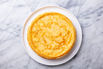 Crepes, thin pancakes on a white plate. Marble background. Copy space. Top view.
