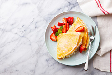 Crepes, thin pancakes with cream cheese, ricotta, fresh strawberries and sugar powder. Marble background. Top view.