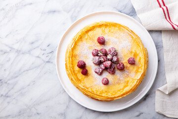 Crepes, thin pancakes with raspberry on white plate. Marble background. Top view. Copy space.