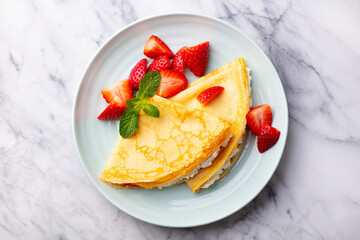 Crepes, thin pancakes with cream cheese, ricotta and fresh strawberries. Marble background. Top view.