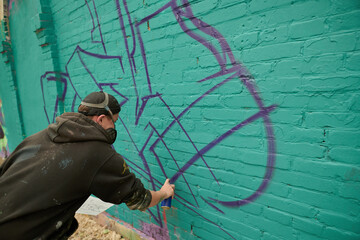 Rear view of young creative man in protective respirator bending forwards and creating new graffiti...
