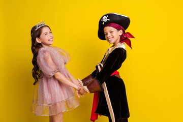 Profile photo of two kids halloween princess pirate costume hold arms empty space isolated on yellow color background