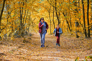Obraz premium A mother and son are jogging through a vibrant autumn forest, surrounded by golden leaves.