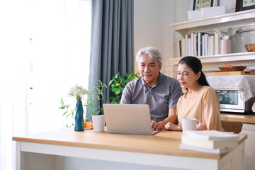 Elderly man and his wife are using laptop to watch a cooking video at the kitchen.