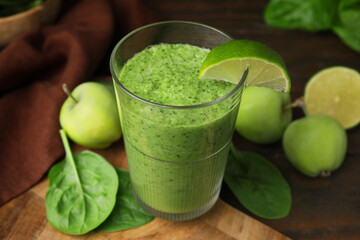 Tasty green smoothie in glass with lime, apples and spinach on wooden table, closeup