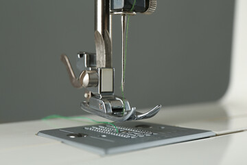 Sewing machine with green thread on grey background, closeup