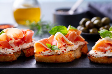 Bruschetta, crostini with Jam?n, ham and fresh basil on dark marble board. Close up.