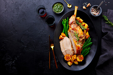 Roasted lamb leg with potato and green peas. Black background. Copy space. Top view. © annapustynnikova