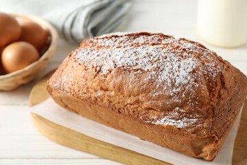 Tasty sponge cake with powdered sugar on white table, closeup