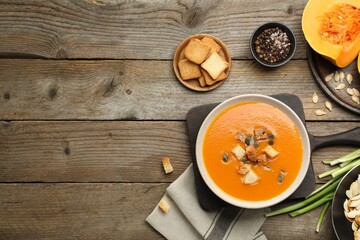 Delicious pumpkin soup in bowl and ingredients on wooden table, flat lay. Space for text