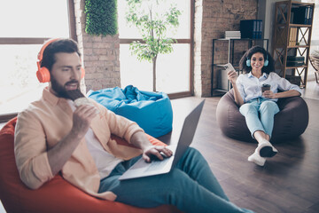 Portrait of two young corporate workers eat chocolate use laptop phone modern loft interior office indoors