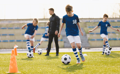 Obraz premium Teenagers on soccer training camp. The boys practice football on a grass pitch. Junior-level athletes improving soccer skills on outdoor training. Player jumping over hurdles and ladder-skipping