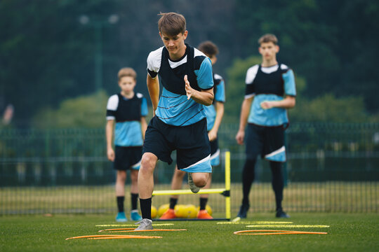 Teenagers on soccer training camp. Boys practice football with young coaches. Junior-level athletes improving soccer skills on outdoor training. The player jumping over hurdles and ladder-skipping