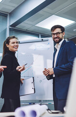 Male and female colleagues collaborating togetherness on new business project feeling great from cooperation in conference room, portrait of cheerful professionals looking at camera near flip chart