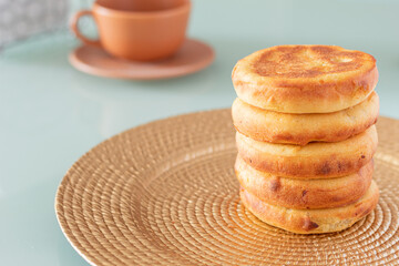 Some arepas from Boyaca, Colombia stacked on a handmade golden plate, an orange cup stands out in the background. Traditional Colombian breakfast.