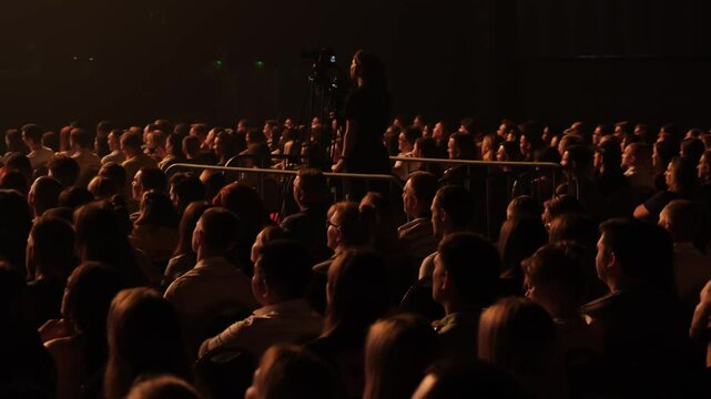 The camera operator films the presenter's performance standing up surrounded by unidentified spectators