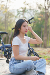 Obraz premium Young asian women wearing earphone and listening audio music on smartphone with happiness while sitting on the street to relaxation with journey travel lifestyle after cycling bicycle in the park