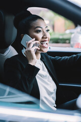 Happy woman in formal wear enjoying road driving in to financial district and online cell call conversation with friend connected to roaming internet in car, cheerful female expert talking via app