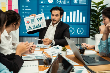 Diverse group of business analyst team analyzing financial data report. Finance data analysis chart and graph dashboard show on TV screen in meeting room for strategic marketing planning. Habiliment