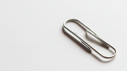 A simple silver paperclip rests on a clean white surface, showcasing minimalism and functionality in office supplies.
