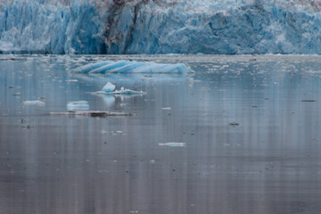 Glacier with floating glacial ice cascading in foreground, streaked reflections cascading vertically into the chilled waters.