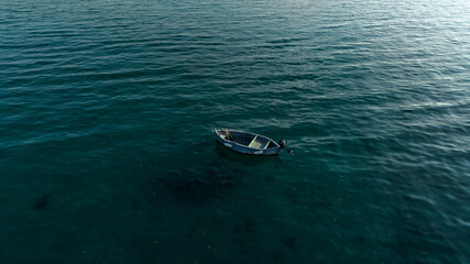 Aerial view of a one small fishing boat anchored in the middle of the sea. The boat is empty and lonely.