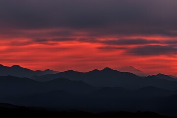 Obraz premium Silhouette of rolling mountains with a vivid red and golden dawn breaking, AI Generated