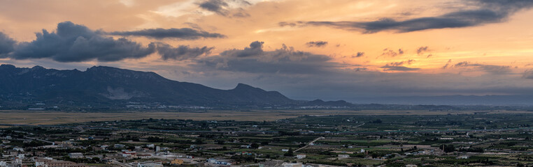 Fototapeta premium A stunning panoramic view of the sunset casting light over mountains and a vast rural landscape, offering a serene and picturesque scene.