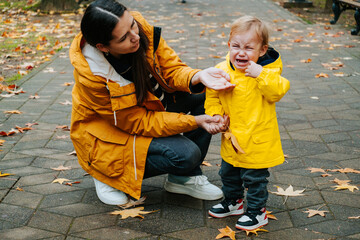 Young mother tries to calm her crying little son outdoor in the park. Raising  child concept.