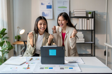 Two businesswomen celebrating success while looking at tablet in office