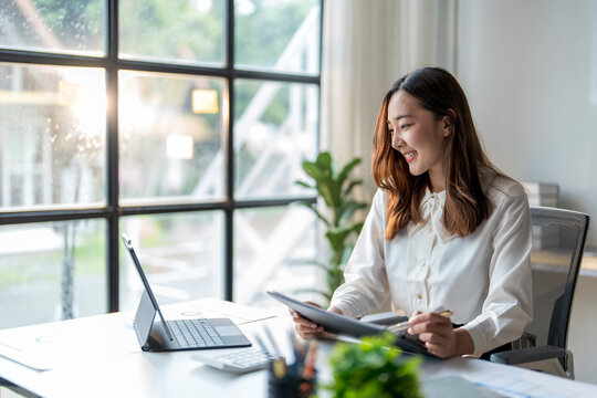 Young asian businesswoman smiling and working on digital tablet at office desk