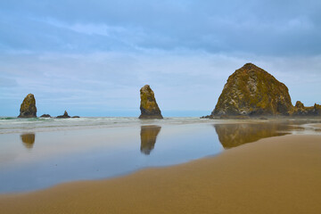 Haystack Rock Reflects In The Low Tide Of Canon Beach On Cloudy Morning.