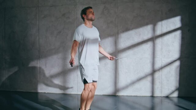 Strong man doing cardio workout with jump rope at loft room. Sportsman jumping