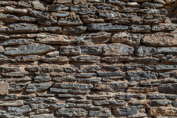 Old ruined masonry made of gray natural stone of different sizes and shapes. Background for design.