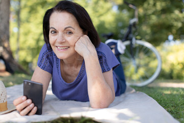 senior woman laying on outdoor sofa and using digital tablet