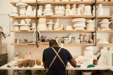 Potter working at a bench under shelves full of ceramic mold