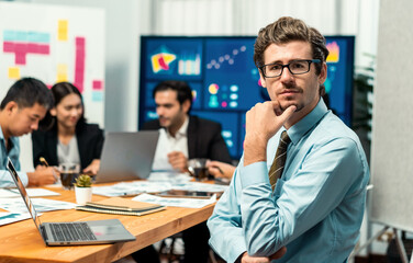 Portrait of businessman or analyst looking at camera with his colleague analyzing data analysis in dynamic business strategy investment planning meeting. Meticulous