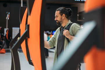 Naklejka premium A man checks in for a plane at the electronic check-in desk. A young tourist guy at the airport gets a ticket at the check-in screen