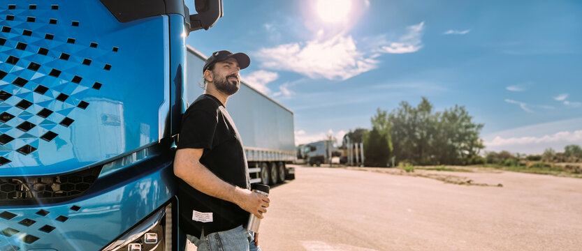 A young man is a professional driver near a blue truck. A handsome guy, a transportation worker stands next to a large truck car